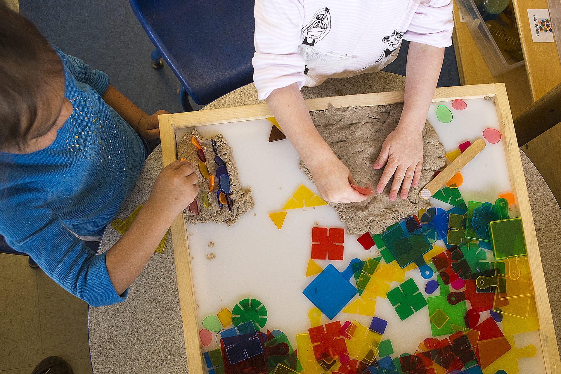 Overhead shot of two children playing with putty and transparent plastic puzzle pieces on a table.