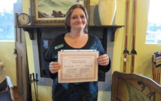 Photo of a woman holding a certificate, indoors, smiling and looking past the camera.