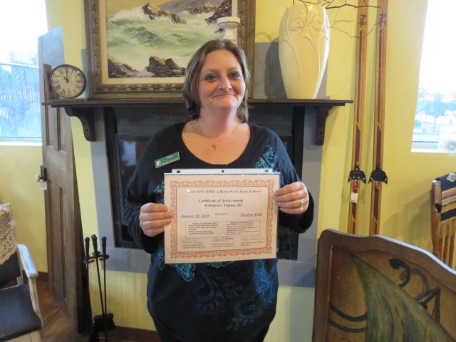 Photo of a woman holding a certificate, indoors, smiling and looking past the camera.