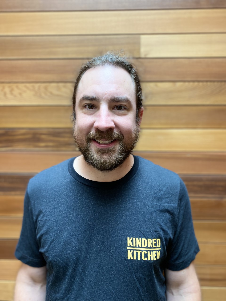 Photo of a man in a Kindred Kitchen t-shirt, smiling at the camera.