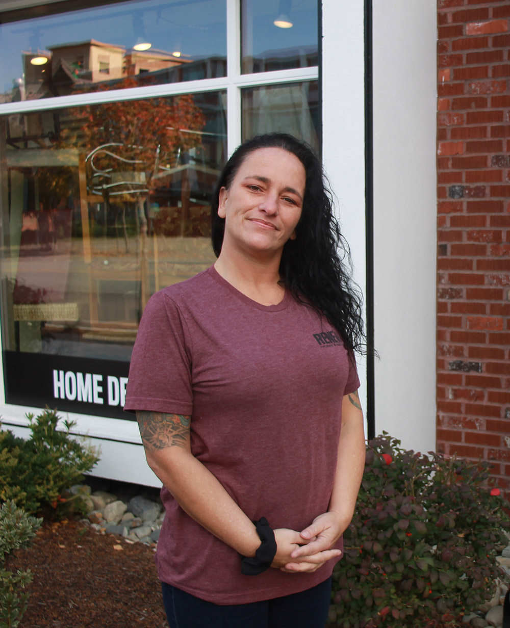 Photo of a woman with tattoos, clasping her hands in front of RENEW Home and Decor.