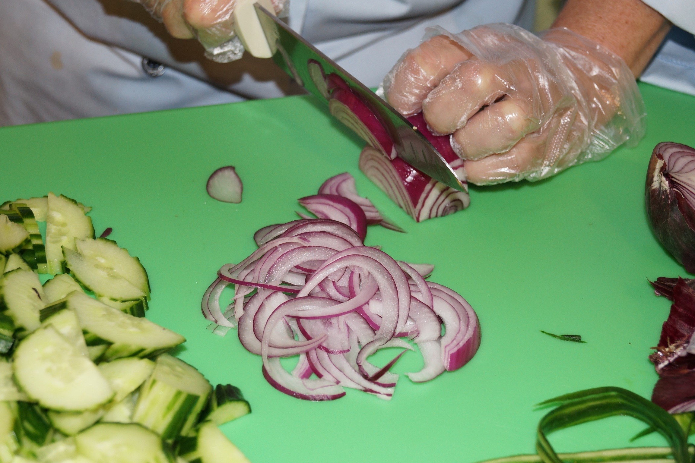 Photo of a person with gloves, cutting red onion on a green cutting board.