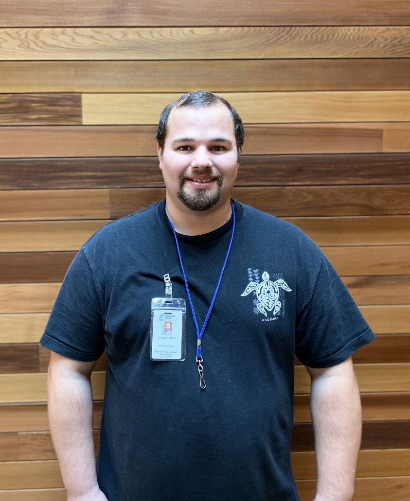 Photo of a man with a goatee and lanyard, standing in front of a wood paneling wall.