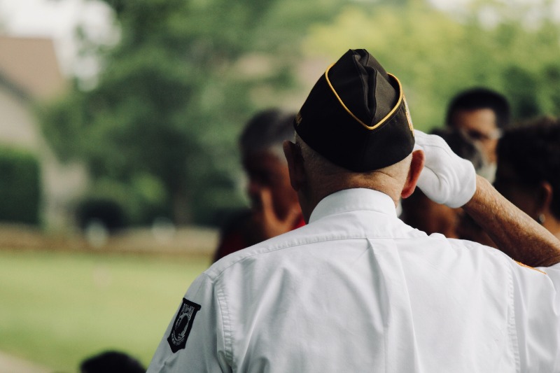 Photo of a veteran saluting, from the back, with others out of focus in front of them.