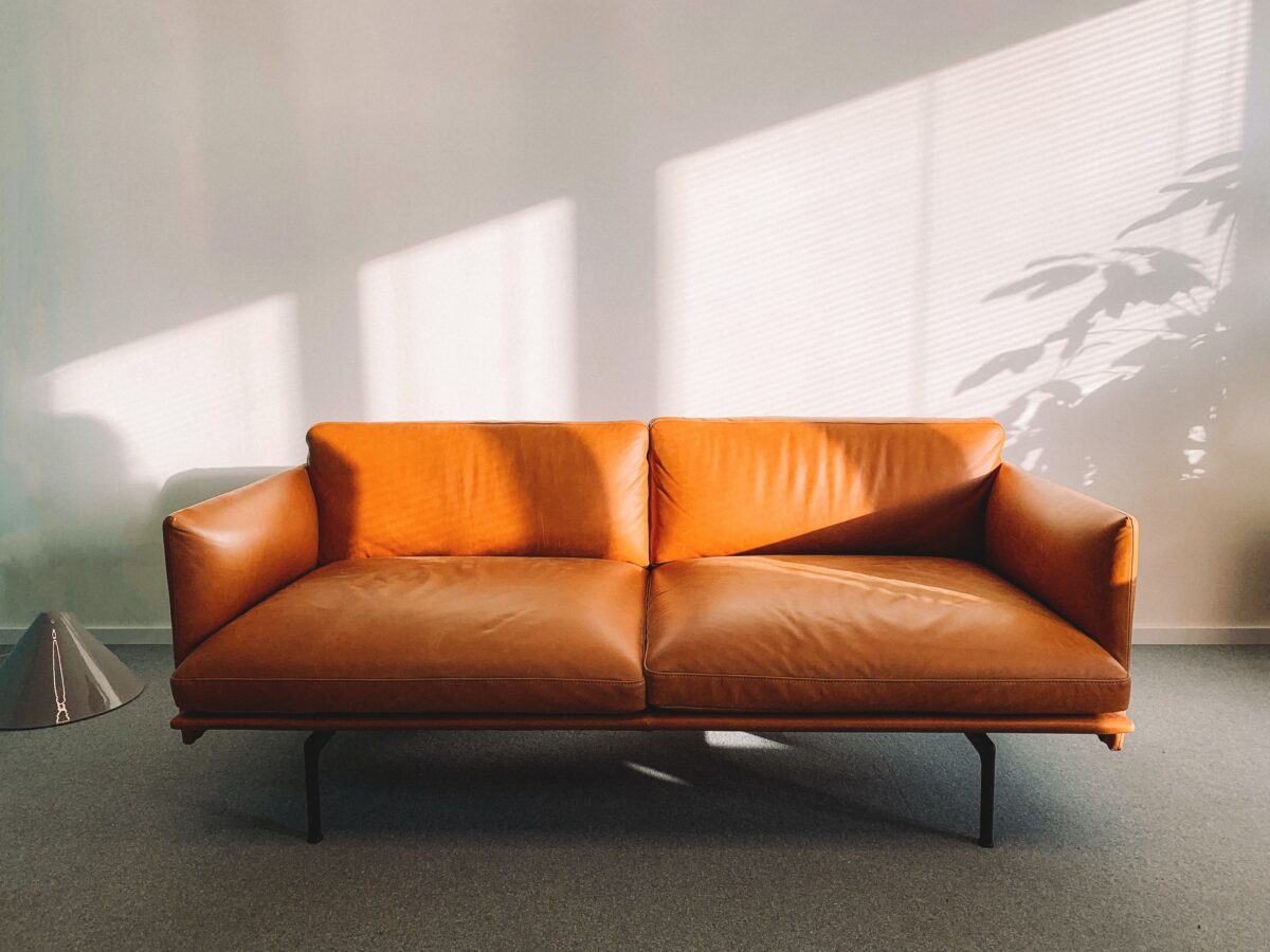 Photo of an orange leather couch, in a white room with office carpet.