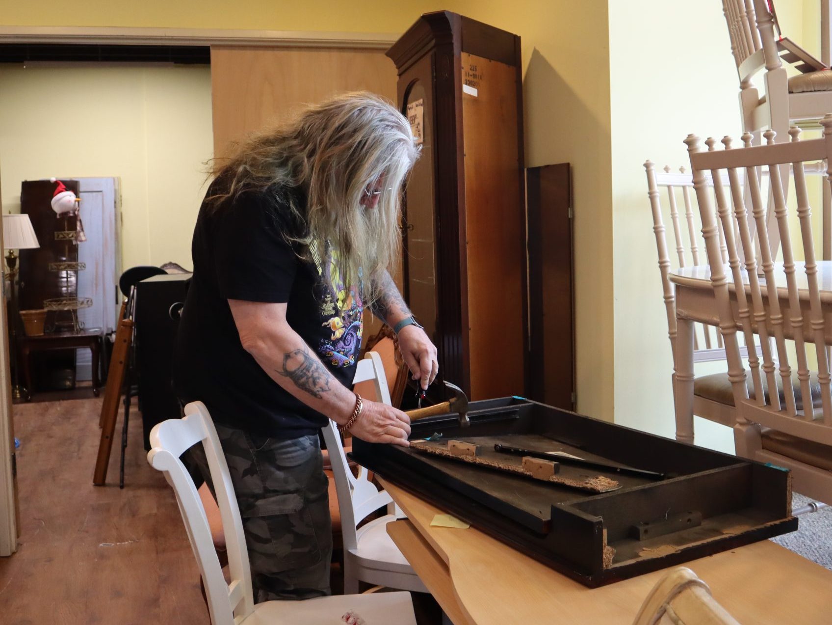 Photo of a man with long gray hair, working on a piece of furniture in a used decor shop.