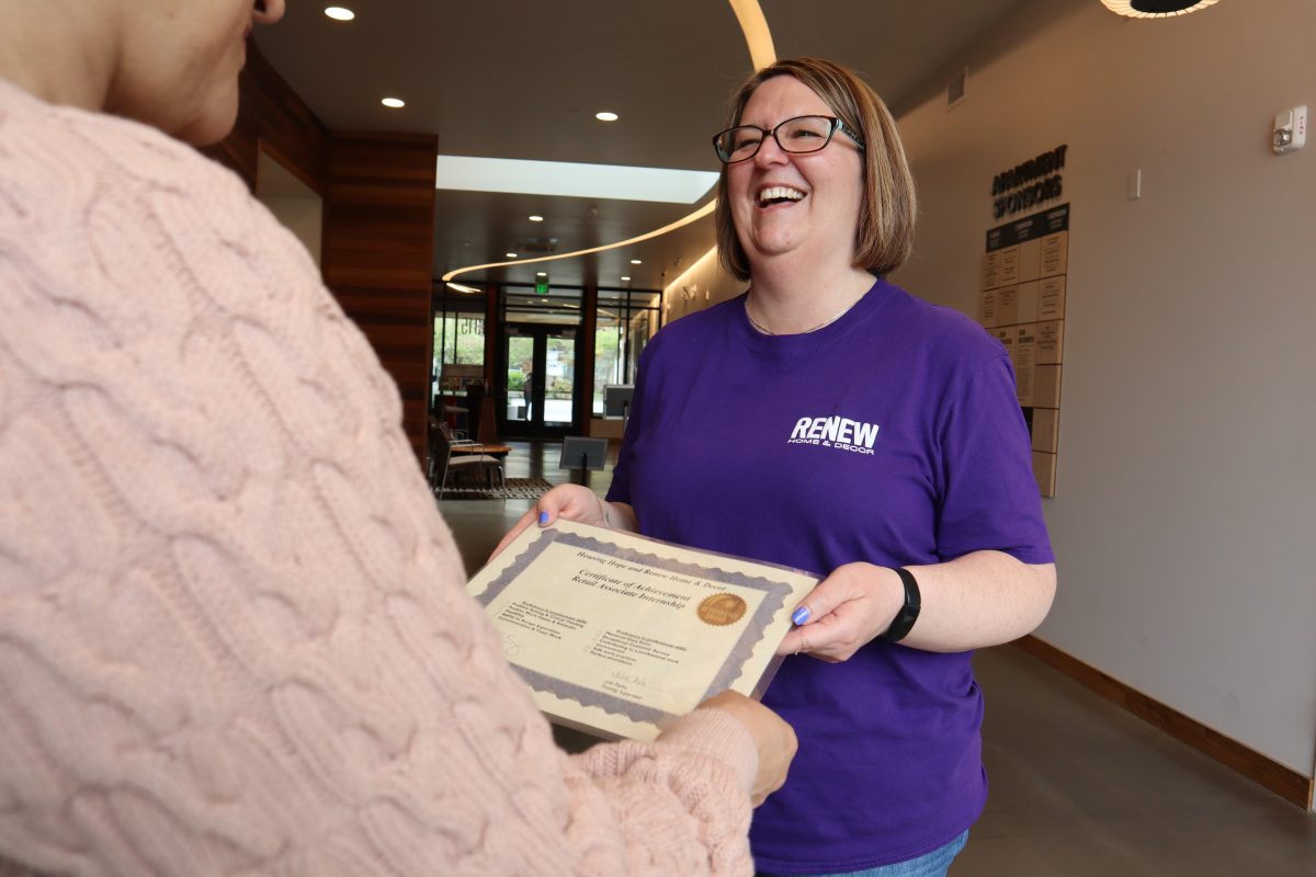 Photo of a smiling woman, handing another woman a graduation certificate.