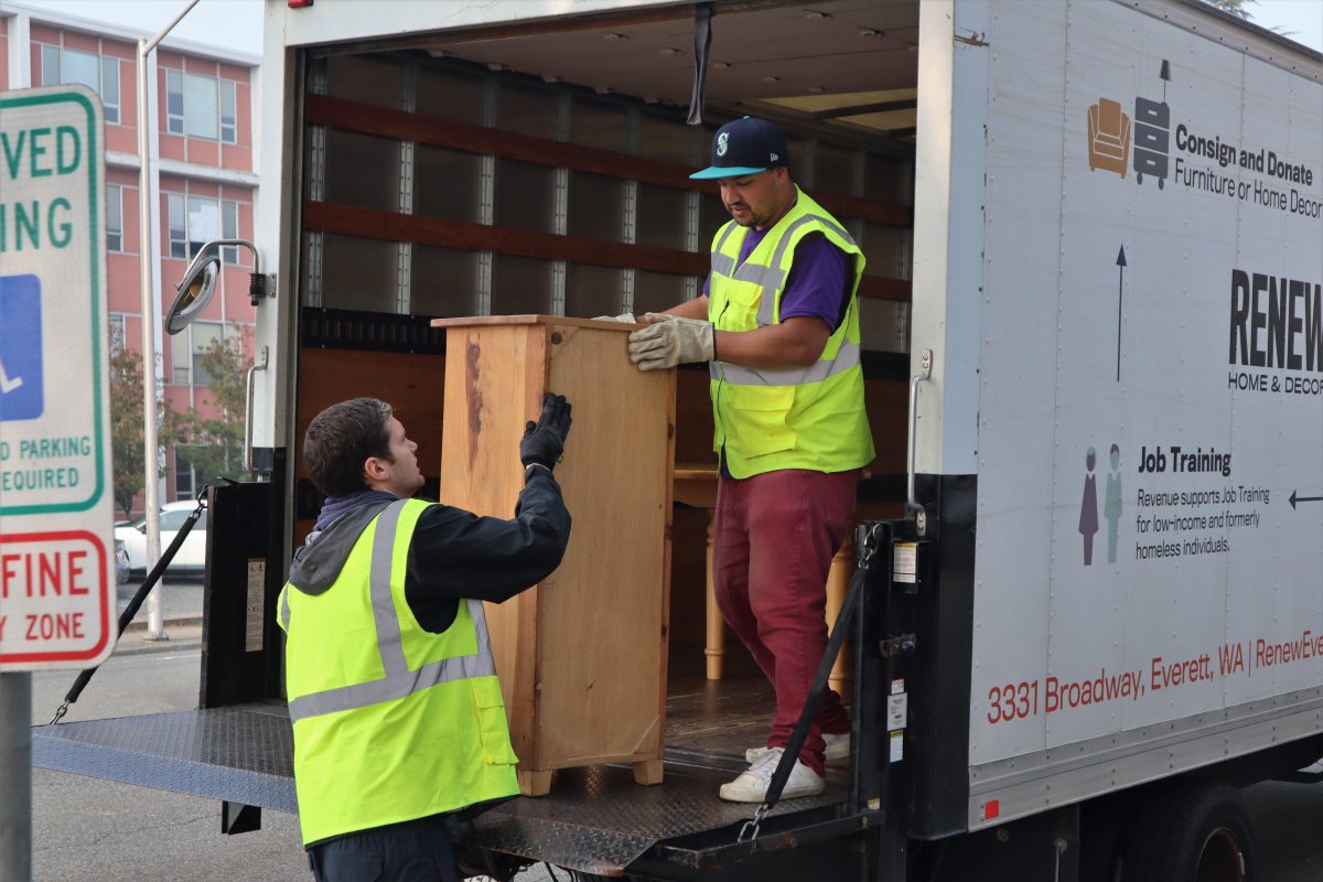 Photo of two men lifting furniture out of the back of a moving truck, in high visibility vests.