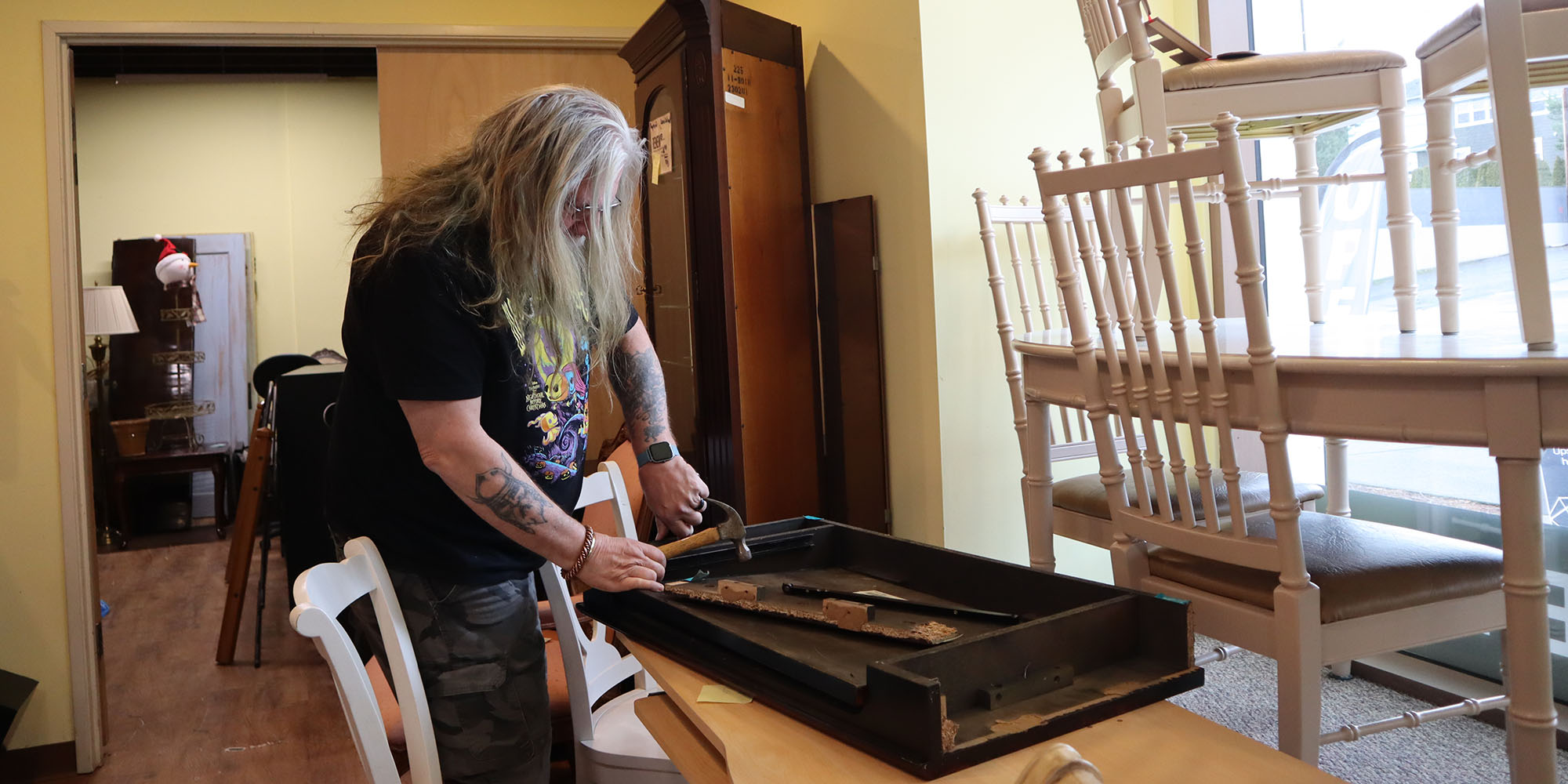 Photo of a man with long hair and beard working with a hammer on a piece of furniture.
